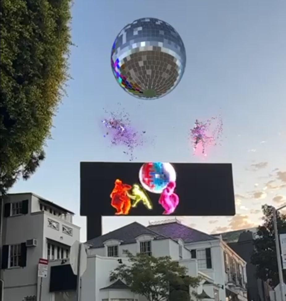 Figures made of colorful bits of paper dance on top of a billboard, while a huge discoball floats overhead